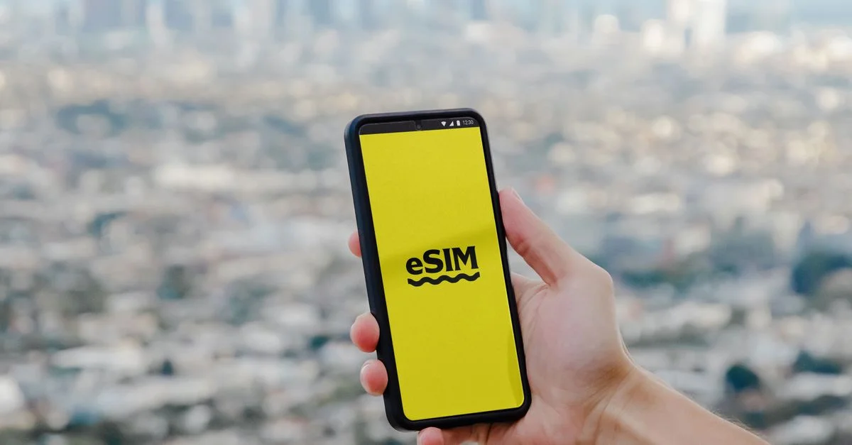 Main tenant un smartphone présentant la technologie eSIM avec une skyline floue de Los Angeles en arrière-plan.