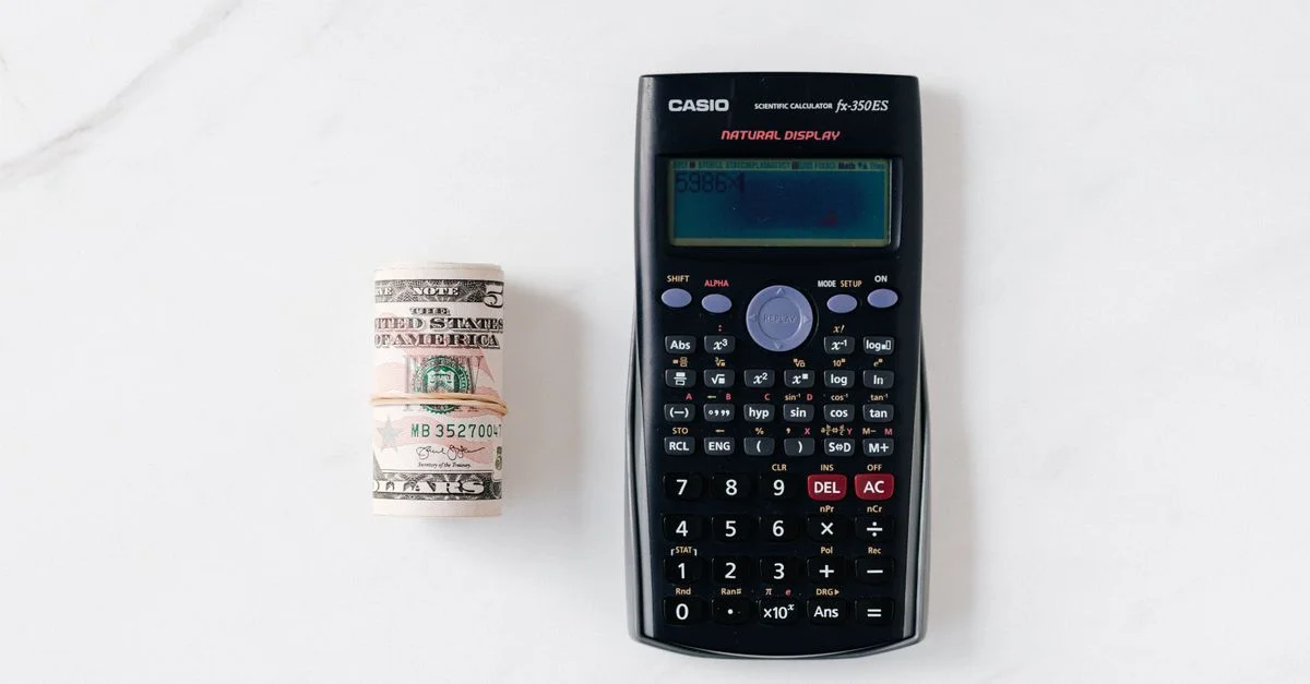 Vue de dessus d'une calculatrice scientifique et d'un rouleau de dollars américains sur une surface en marbre.